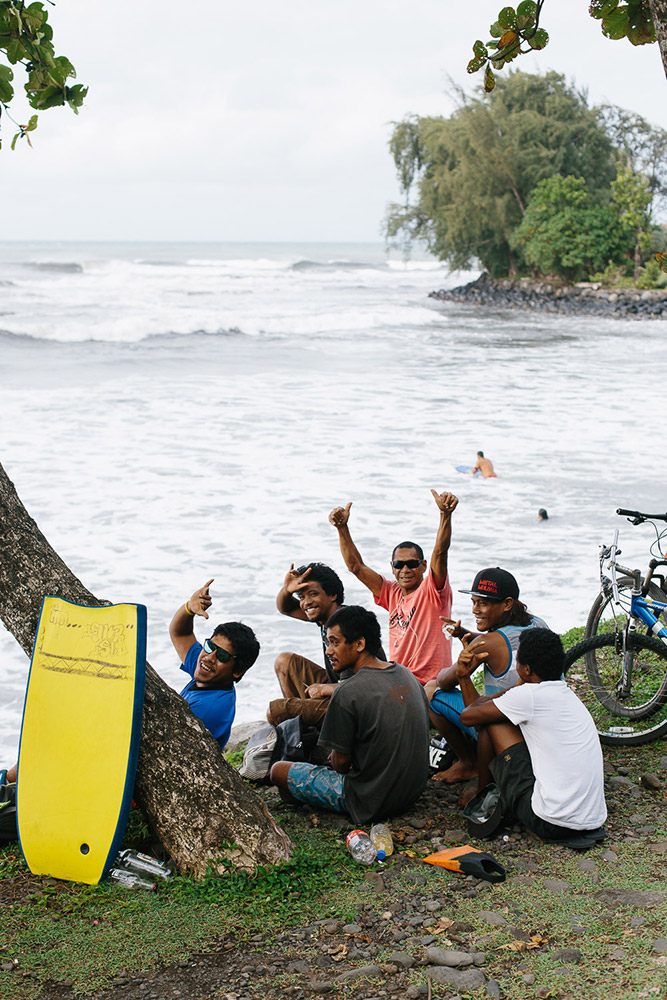 A group of friends watch local surfers off the coast of Tahiti