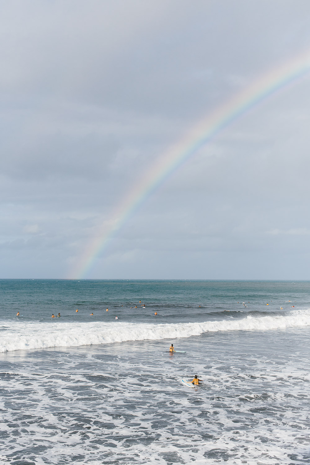 Surfers swim under a rainbow
