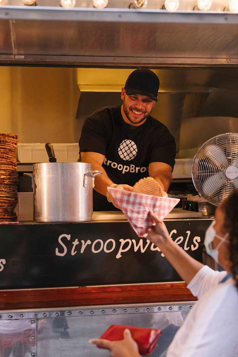 A man smiles serving a customer a Stroopwafel at The Finders Keepers food trucks