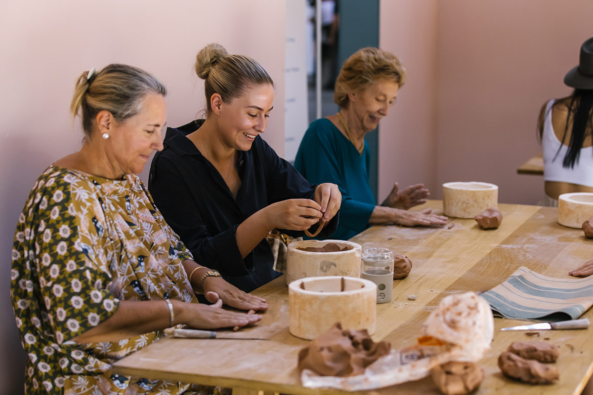 Three women smile as they learn the art of hand building pottery at a ceramics workshop