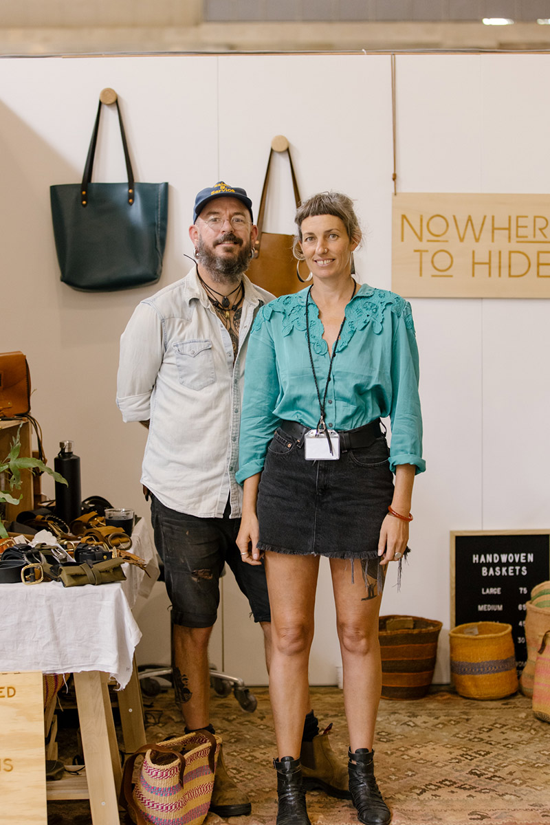 Designers of Nowhere to Hide post for a portrait in front of their stand of handmade leather goods