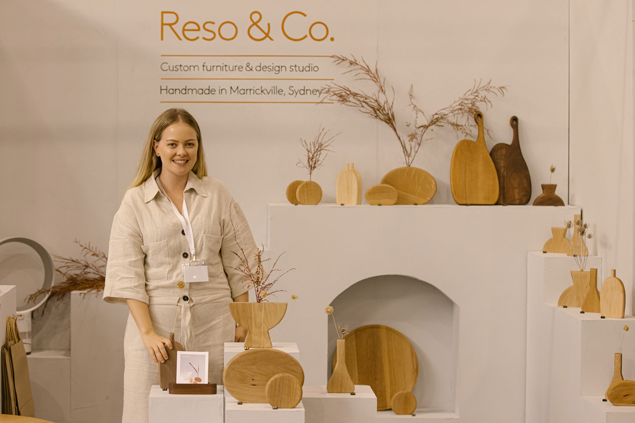 Designers of Reso & Co poses for a portrait with their stand of handmade wooden homewares