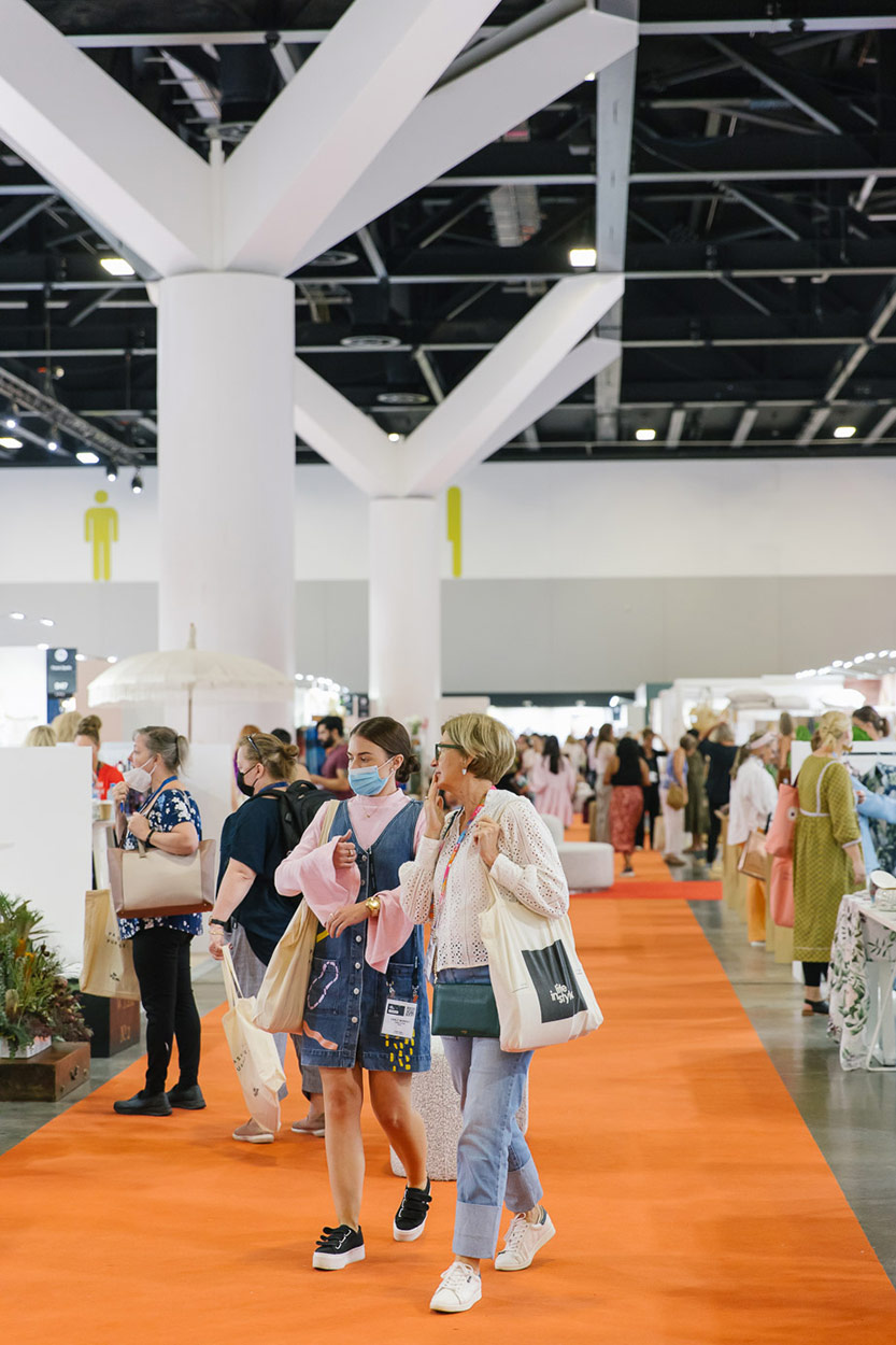 Attendees walk down the bright carpeted aisle at Life Instyle trade show looking to source products