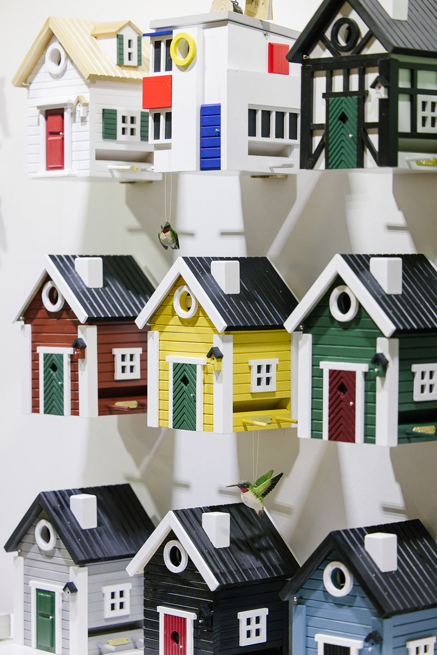 Nine brightly coloured wooden bird houses mounted for display on a white wall
