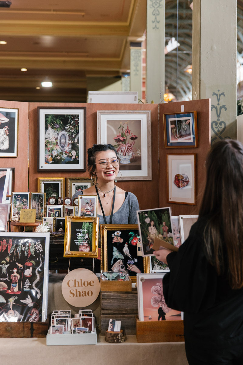 Designer stands at their stall of illustrated prints and framed works for sale at The Finders Keepers Market Melbourne
