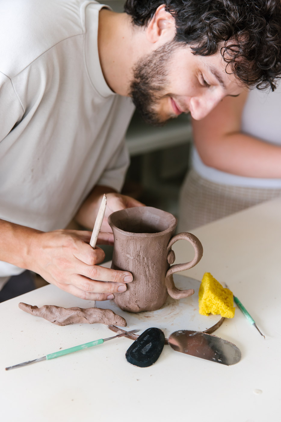 During a hand building ceramics class a student is making a tall mug with a curly handle