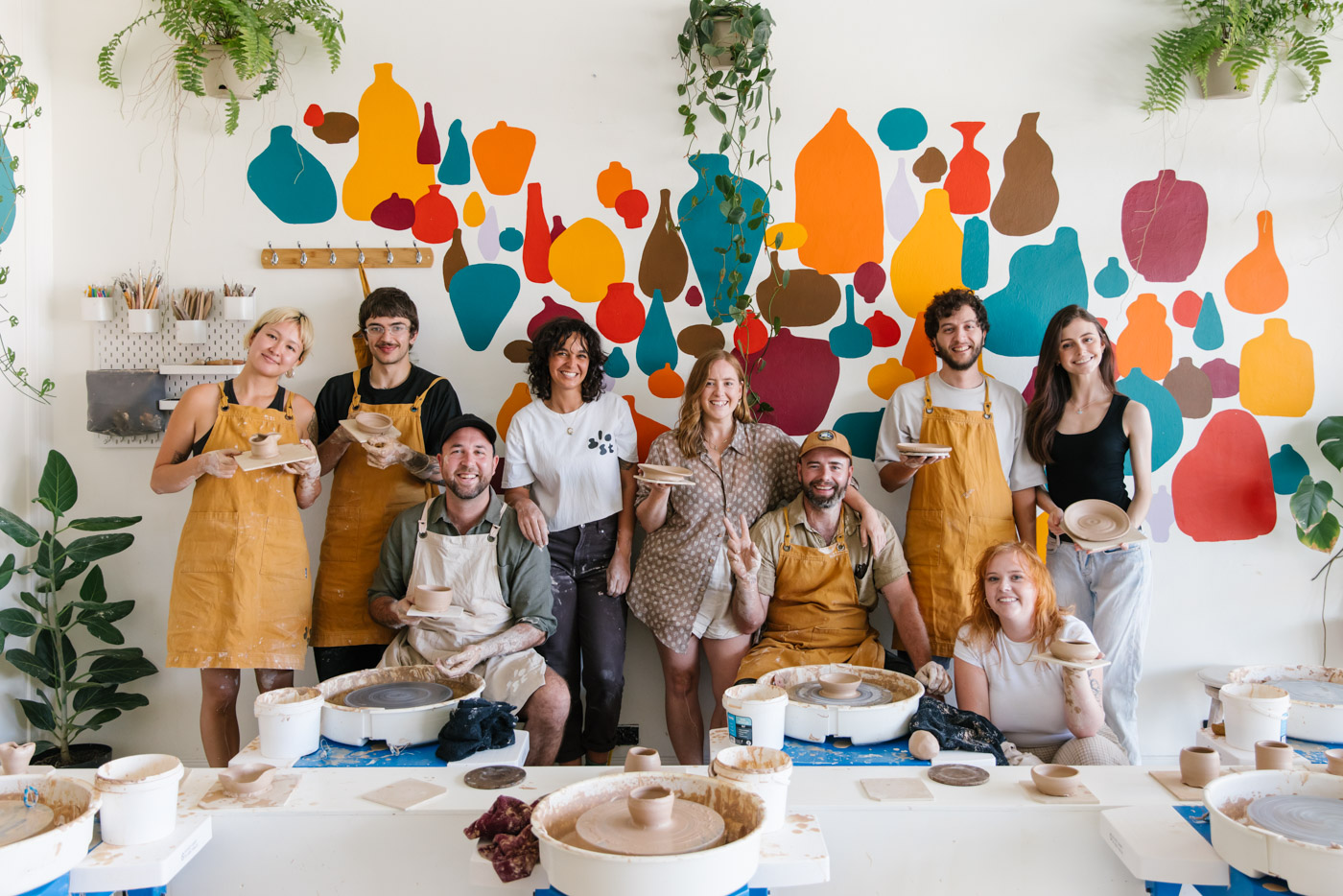 Students of a wheel throwing ceramics class pose for a photo with the pieces they made at Glost Studio Sydney