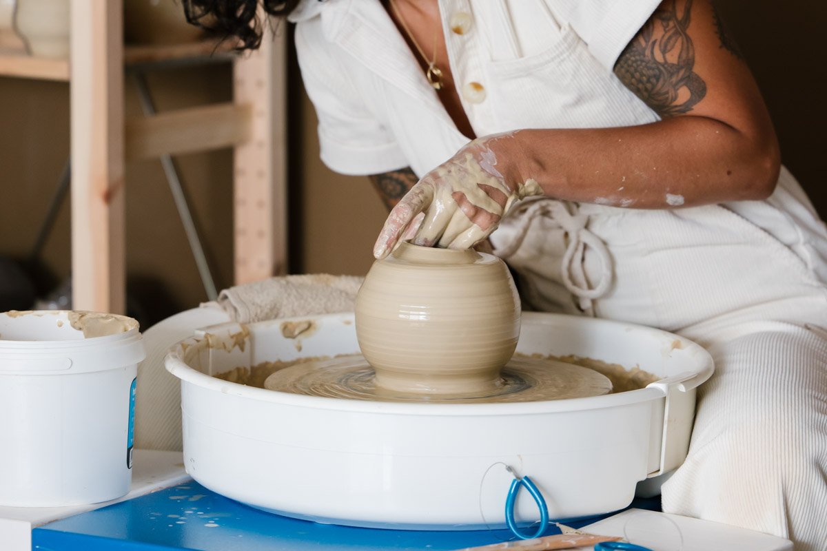 A women throws a rounded vase on a pottery wheel