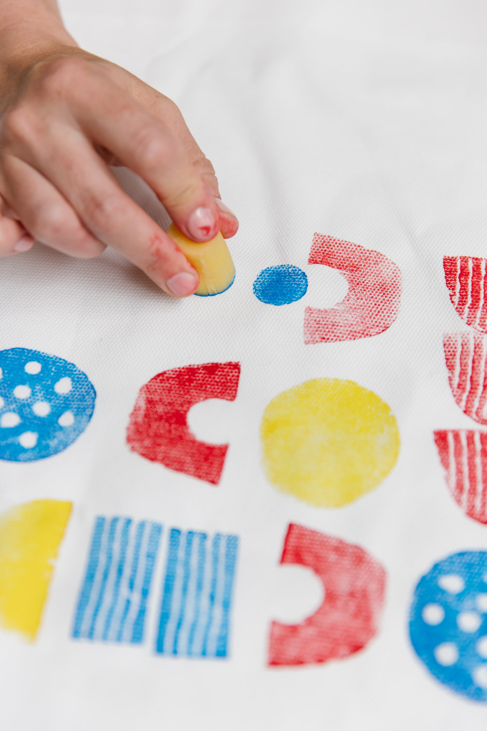 Printing with potato shapes onto a tote bag in bright primary colours