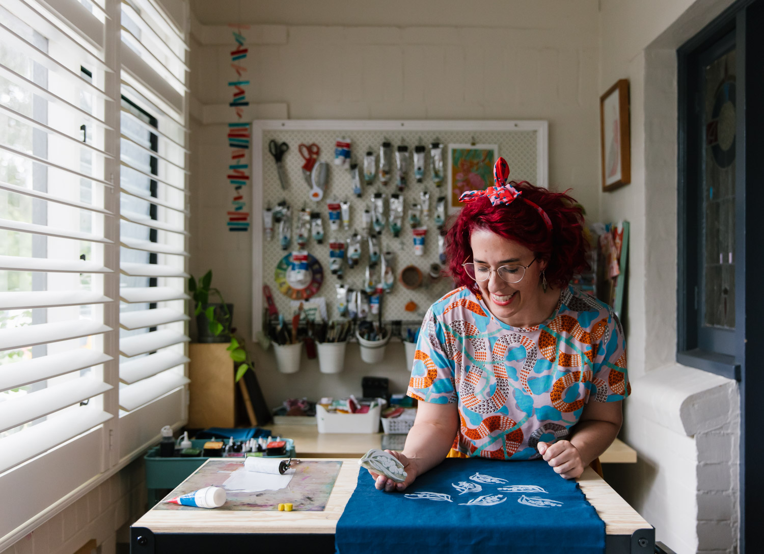 Portrait of a woman laughing while she block prints by hand onto navy fabric in her creative studio space