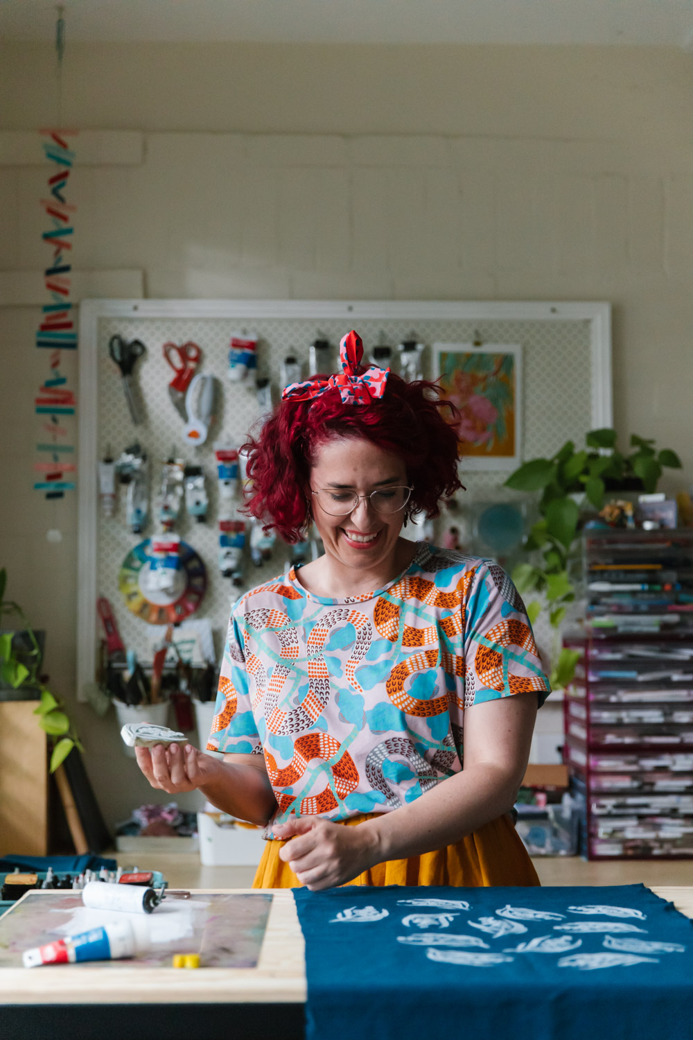 Portrait of a woman laughing while she block prints by hand onto navy fabric in her creative studio space