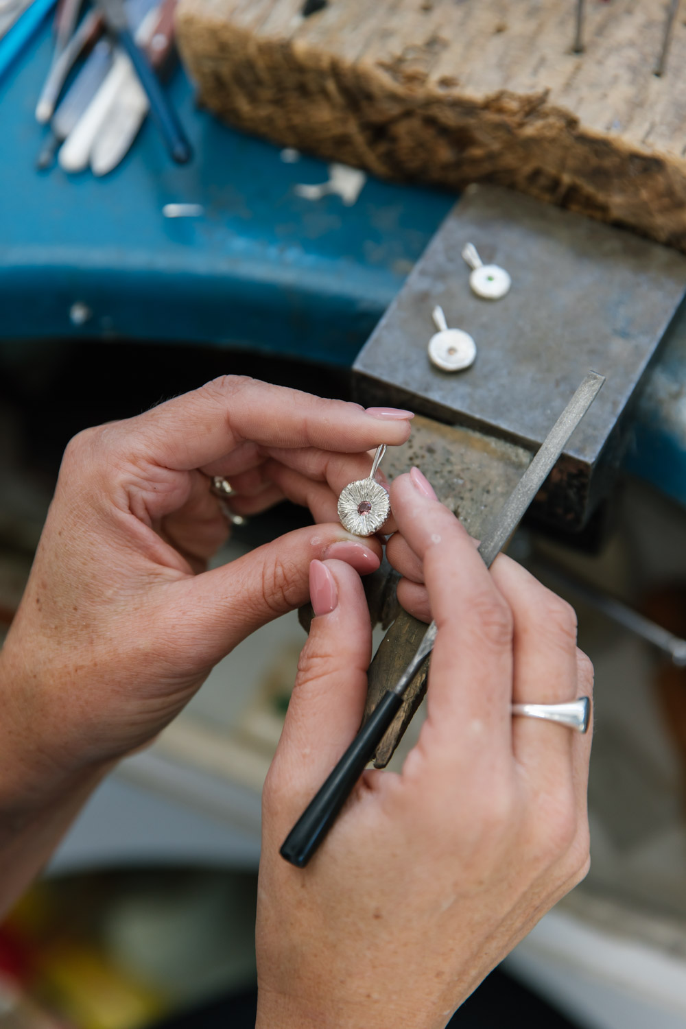 Close up of a jewellers workbench as they file a round necklace pendant in sterling silver featuring a pink gemstone