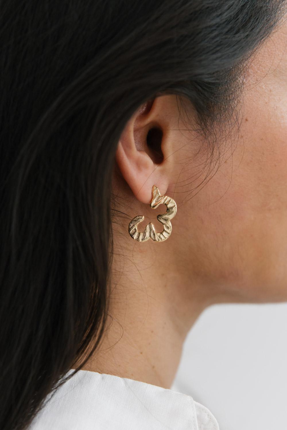 Detail of a single gold daisy earring design on the right ear of a woman of colour
