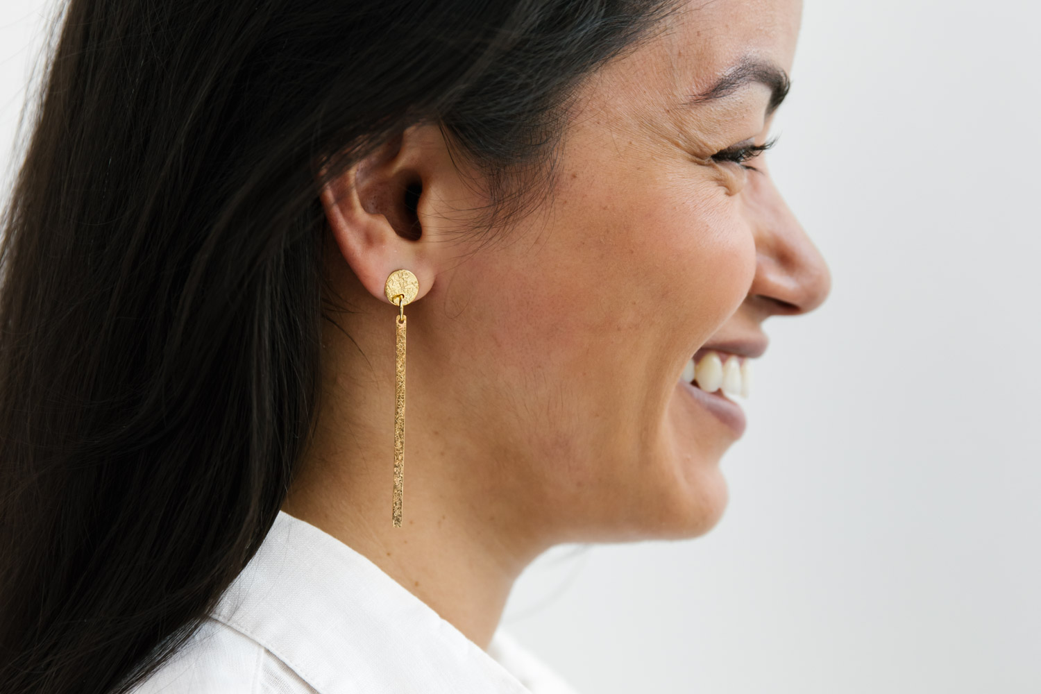 Profile of a woman of colour, smiling and wearing long gold earrings
