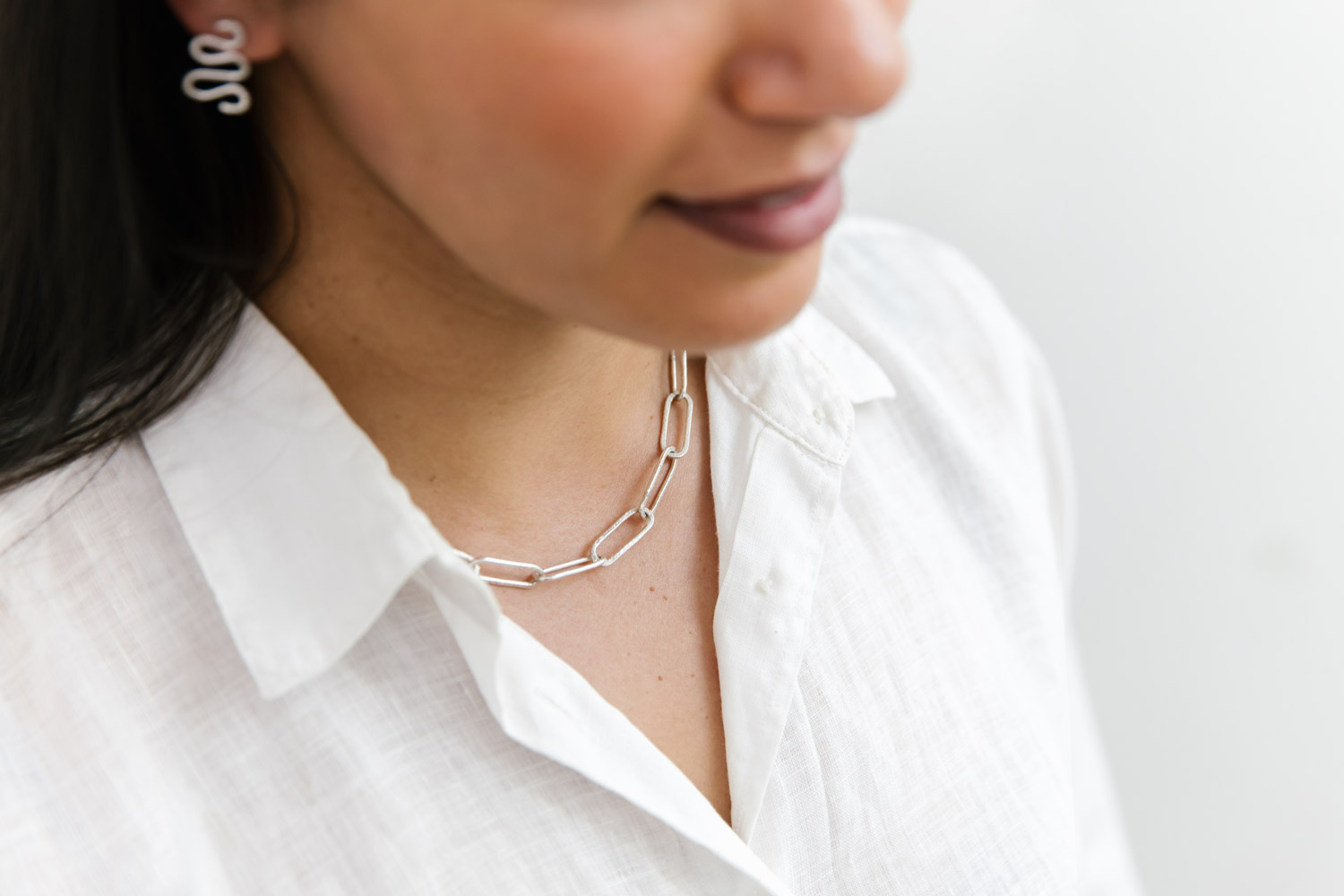 A women of colour wears a white linen shirt and a sterling silver change necklace