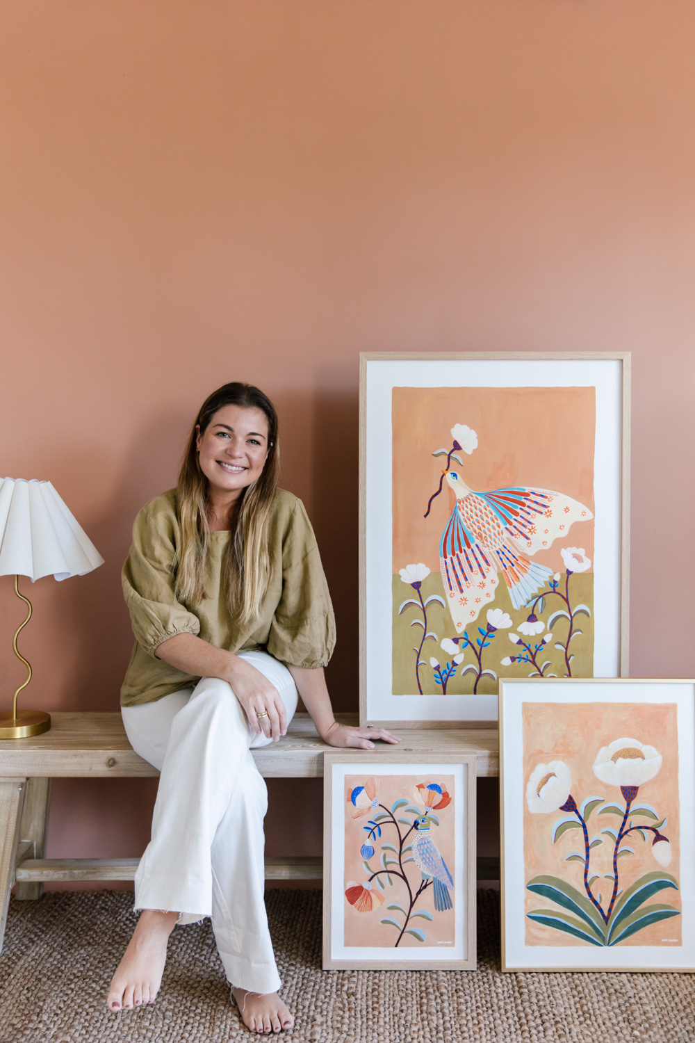 Portrait of artist Karina Jambrak sitting alongside three of her framed works, photo by Samee Lapham
