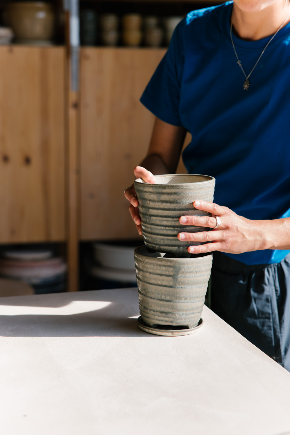 Ceramic planters stacked together in the hands of Melody Brunton as she arranges the studio in the morning sun